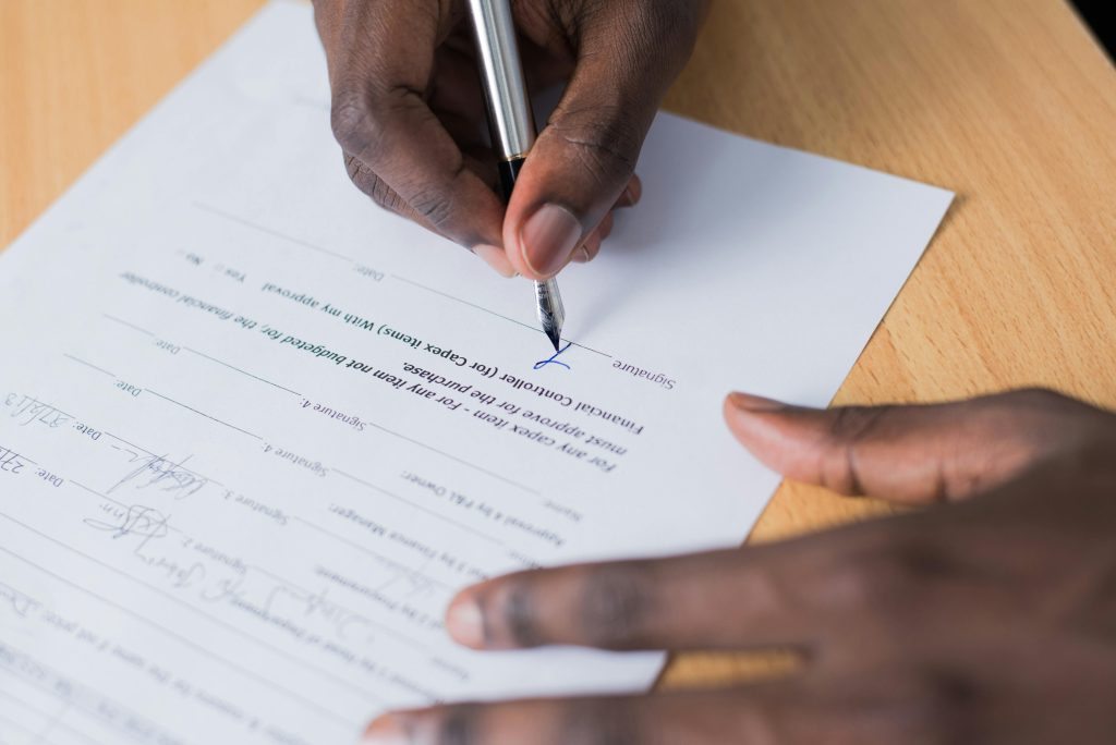 A close-up view of a person's hand signing a business contract on a desk with a pen.